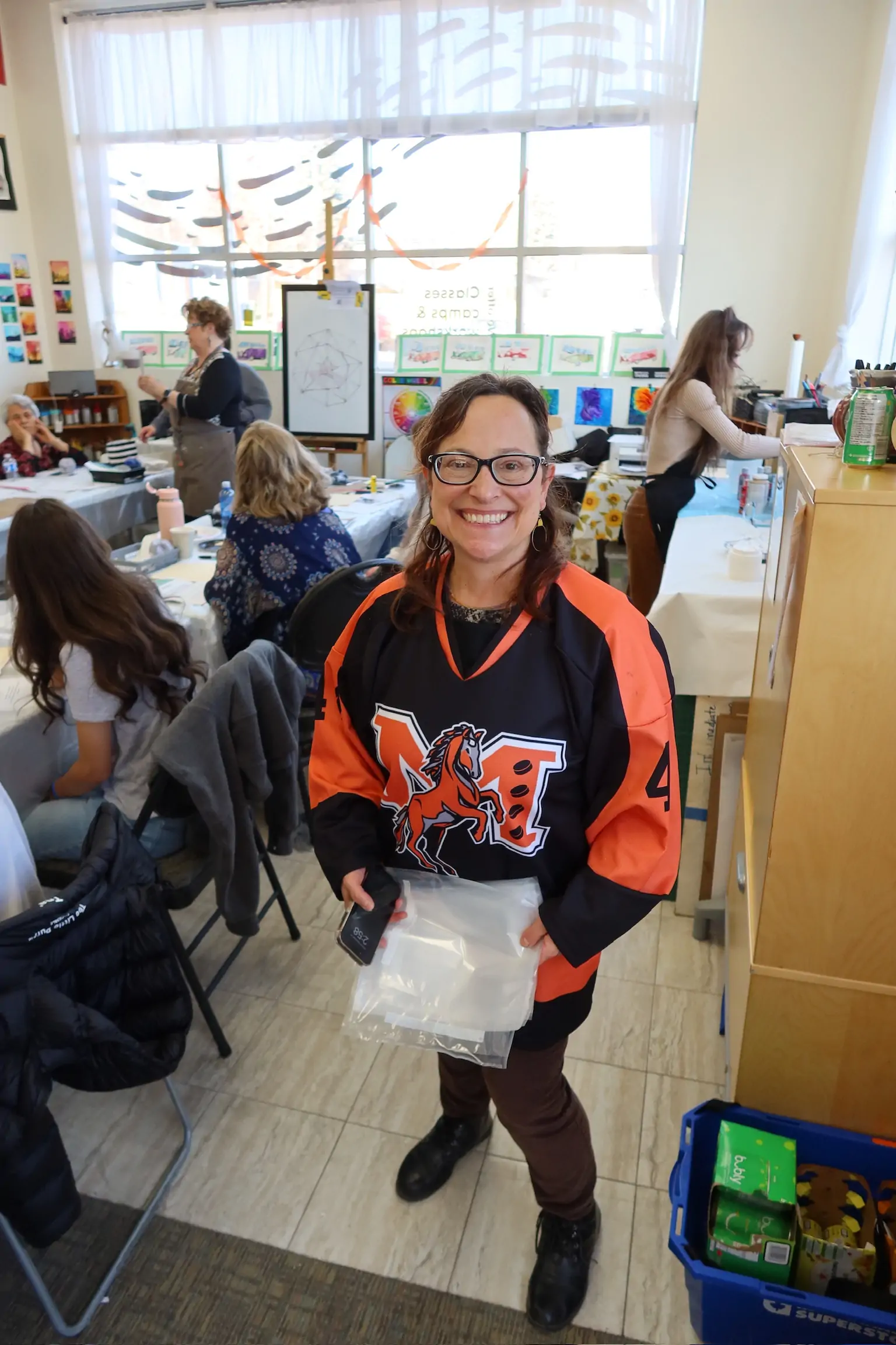 Diana smiling and standing at an art workshop with participants working in the background