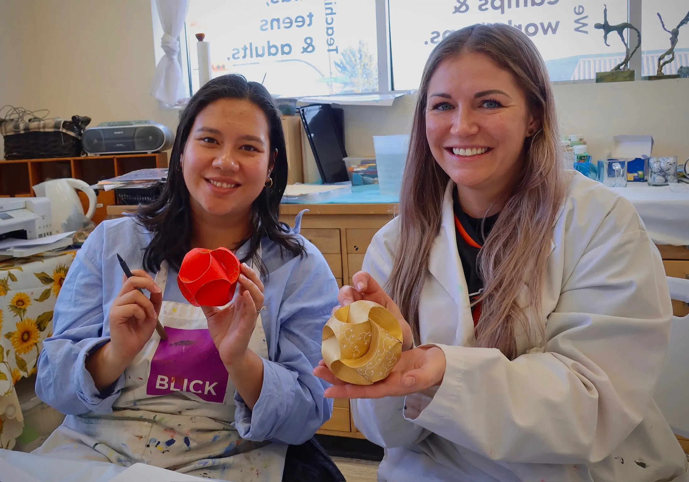 two adult students smiling and holding spherical paper sculptures during an art workshop at Aliki’s Art House in Calgary