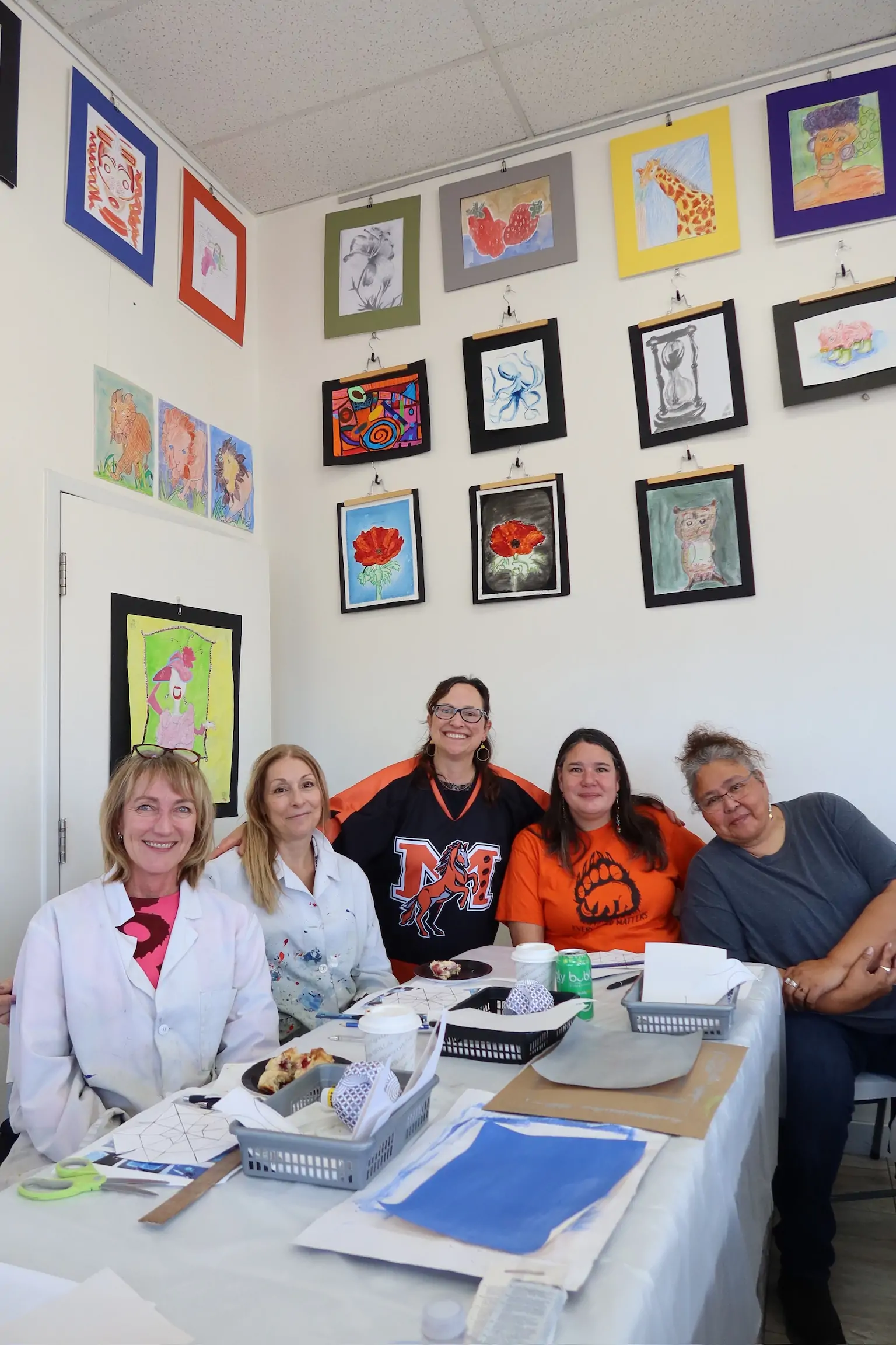 group of workshop participants sitting together at a table during a class at Aliki’s Art House, with Diana seated at the center and student artwork displayed on the wall behind them