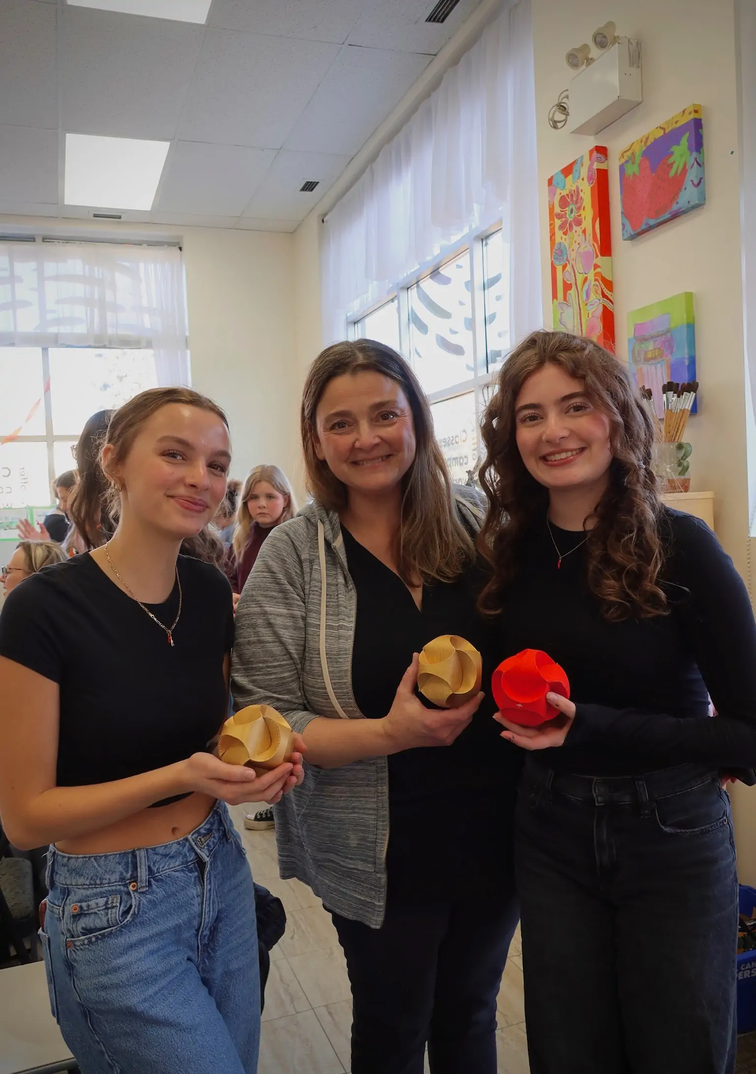 three participants smiling and holding their folded paper art creations during a workshop at Aliki’s Art House