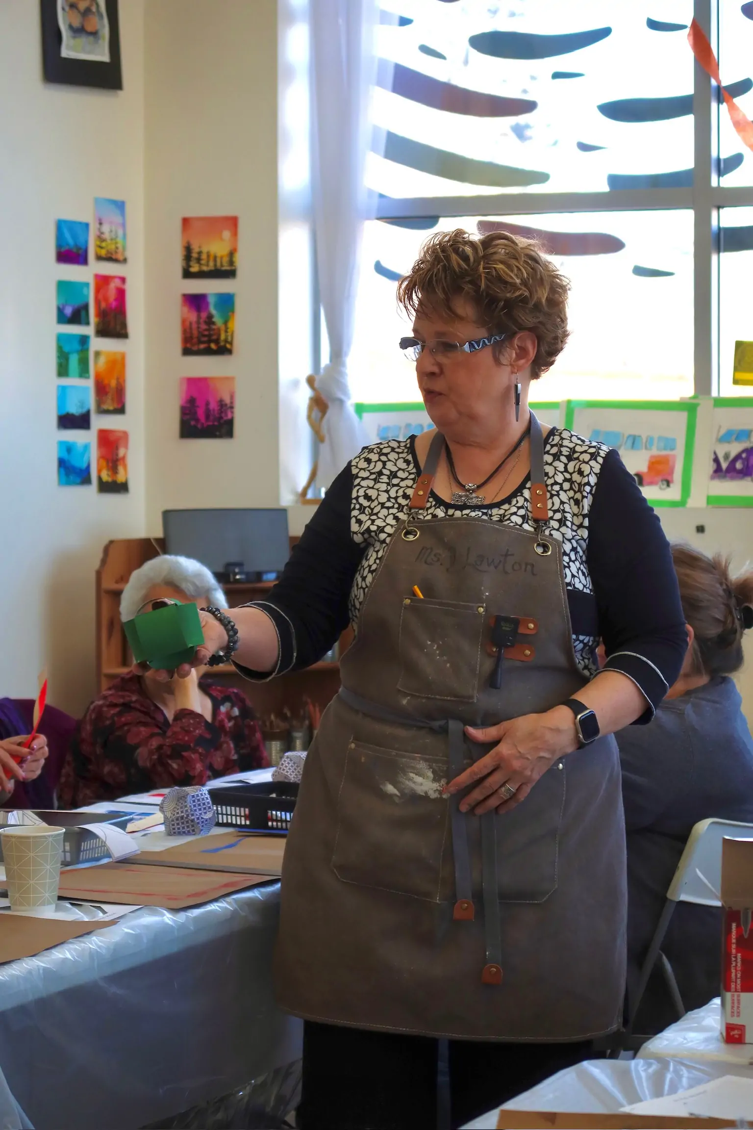 Deborah teaching an art session and demonstrating a technique while holding a small green paper model