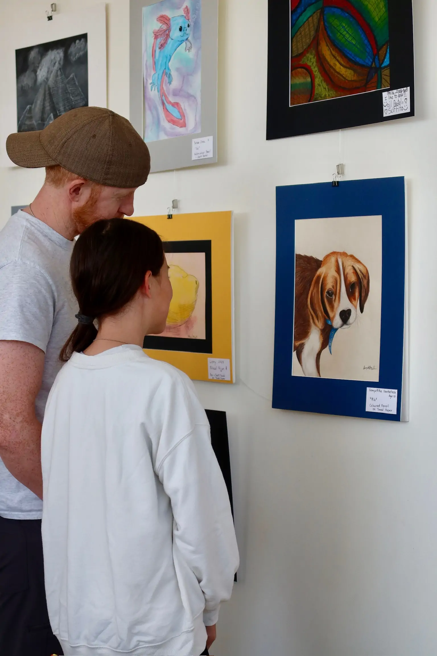 A parent and child view framed student artwork on the wall during the Aliki’s Art House showcase.