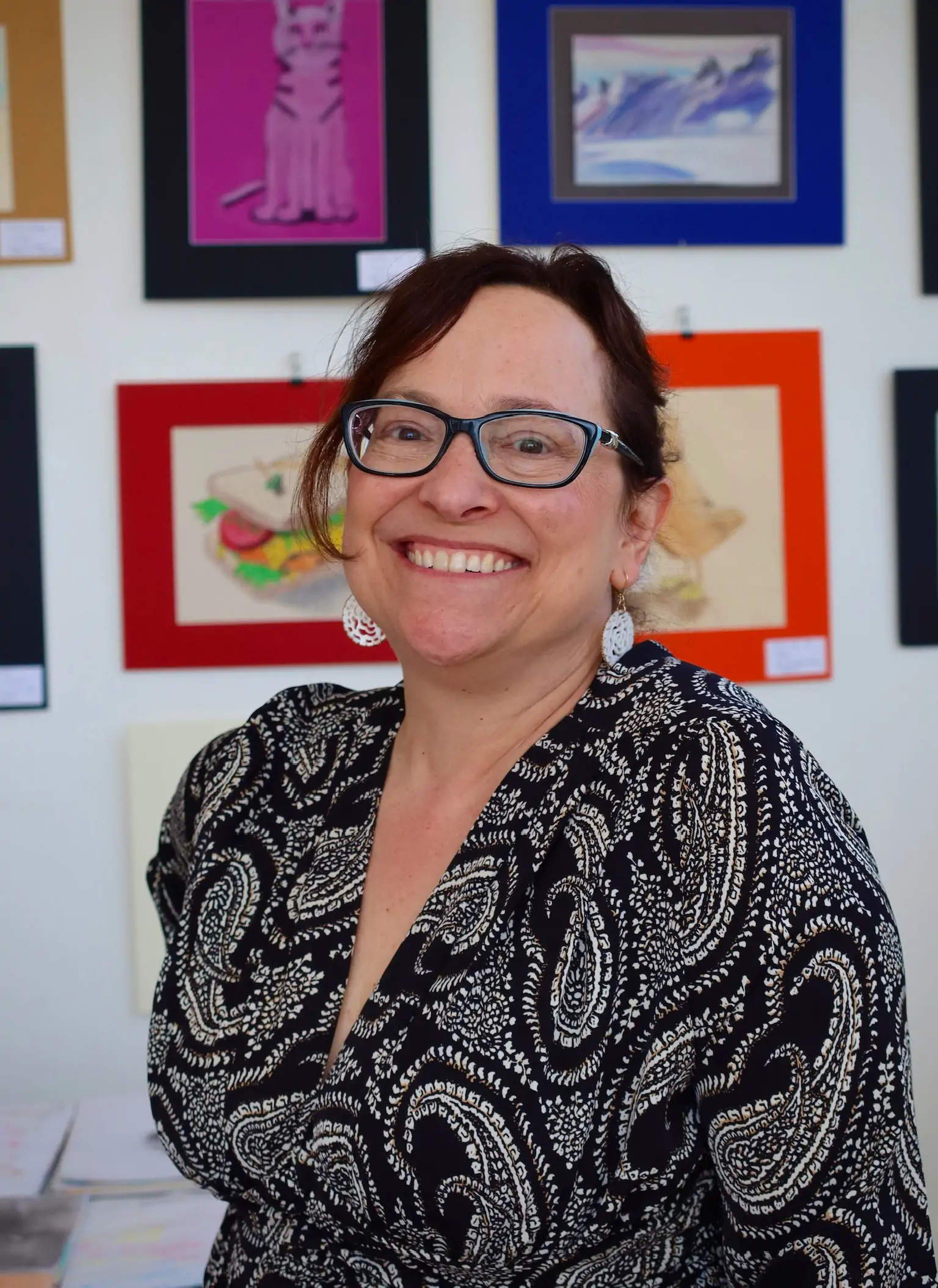 Diana Didrikson, MSc, SLP, owner and studio manager of Aliki’s Art House in Calgary, smiling in front of children’s artwork at the studio