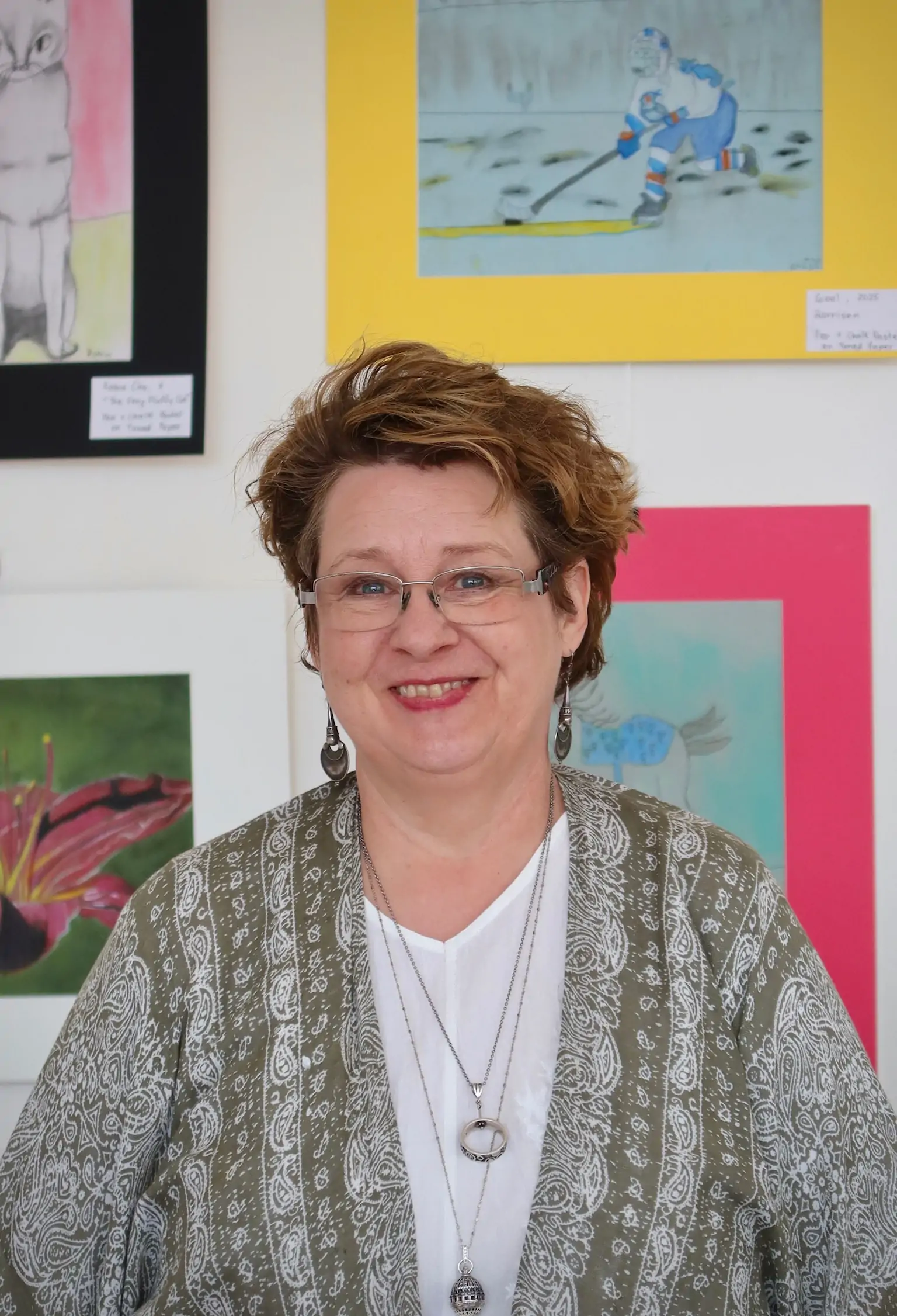 Deborah Lawton, Bachelor of Fine Arts graduate in Sculpture and educator at Aliki’s Art House in Calgary, smiling in front of colorful student artwork