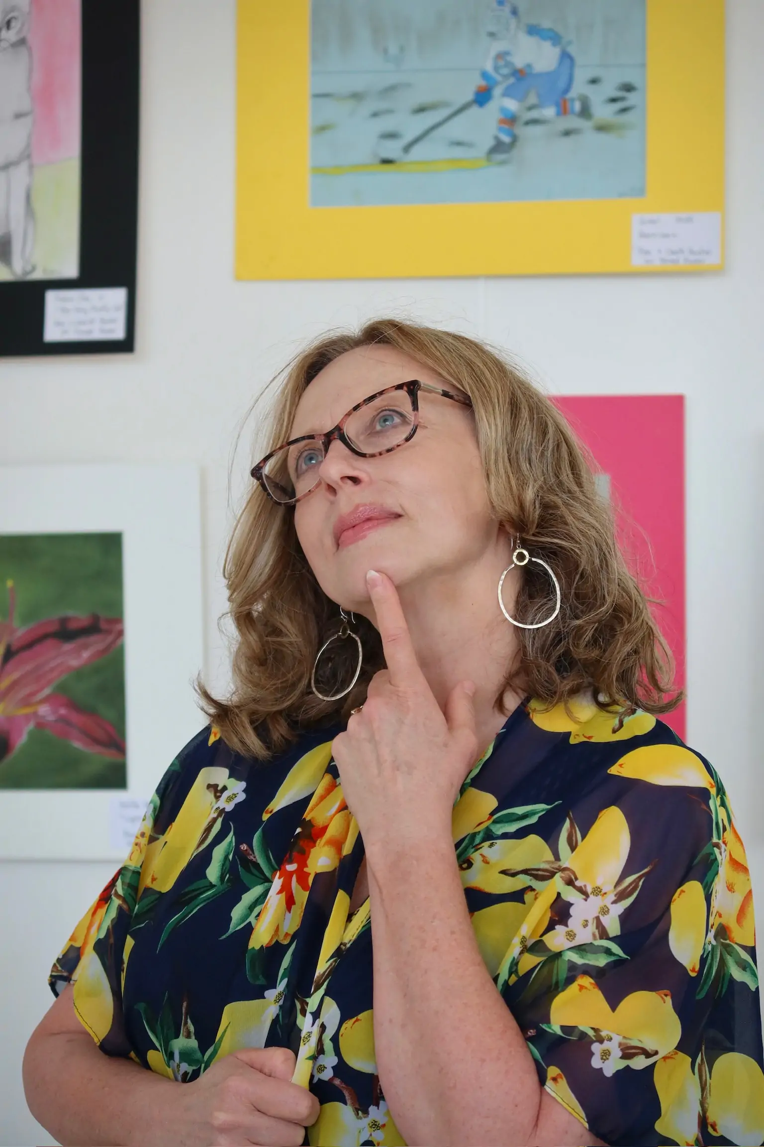 Penny Atkins, artist and teacher at Aliki’s Art House in Calgary, posing thoughtfully in front of colorful student artwork