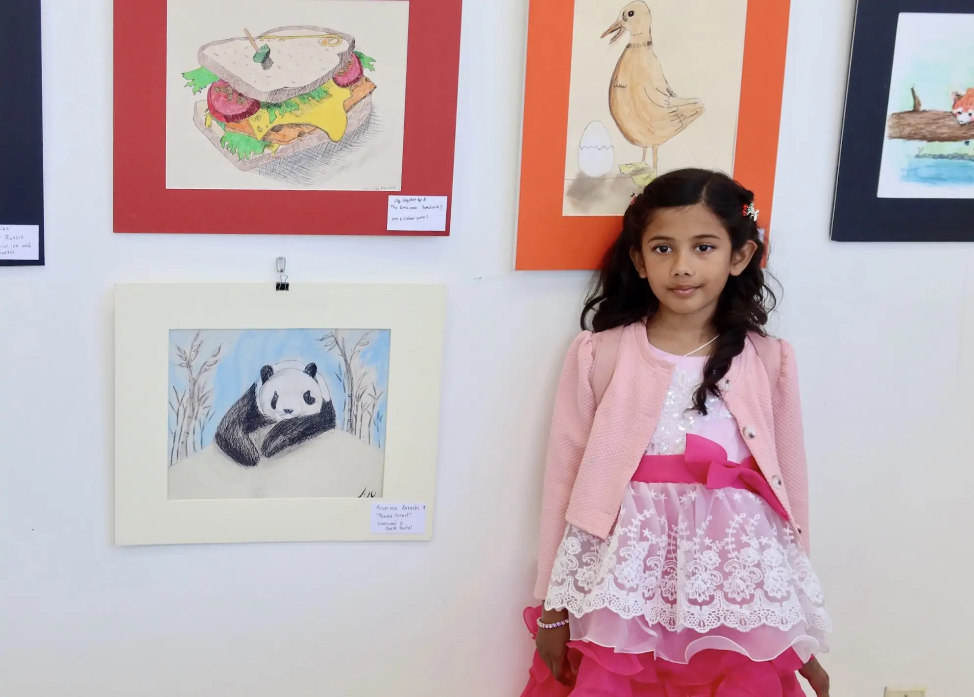 Young student standing beside her panda drawing at the Aliki’s Art House Art Show.