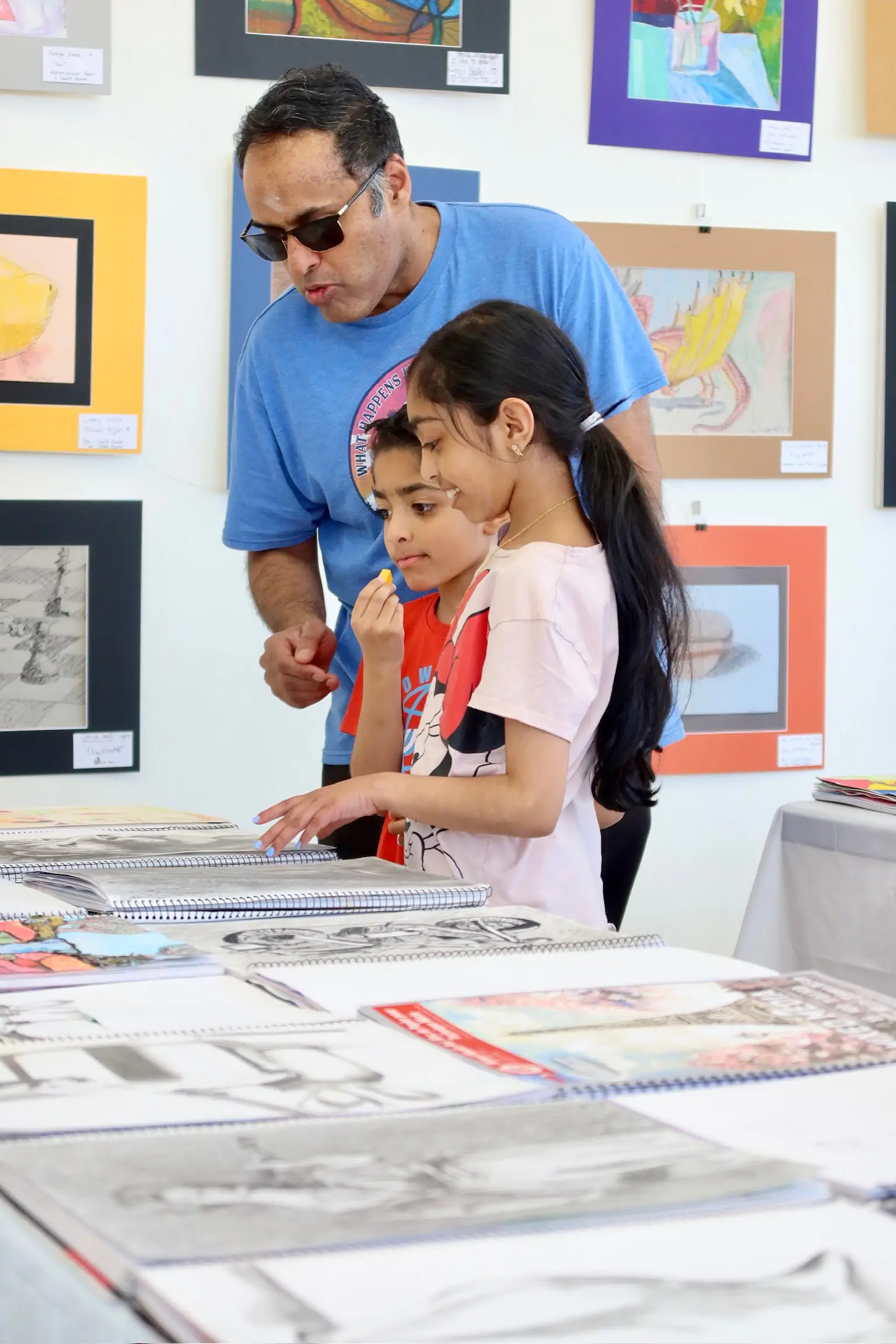 A parent and two children reviewing artwork displayed on a table during a kids’ art class at Aliki’s Art House.