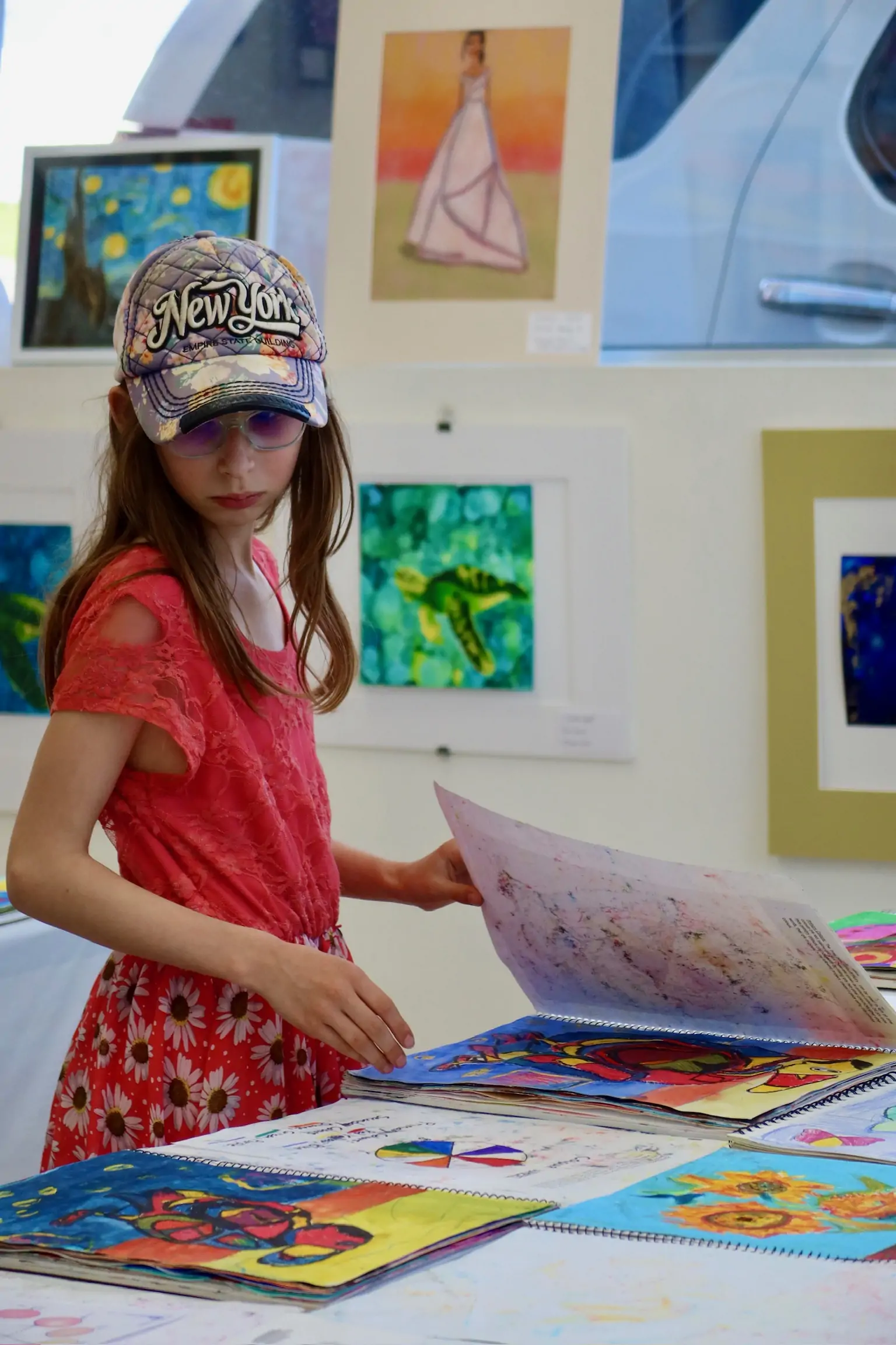 A young student in a red dress looks through her artwork during a children’s art class at Aliki’s Art House.