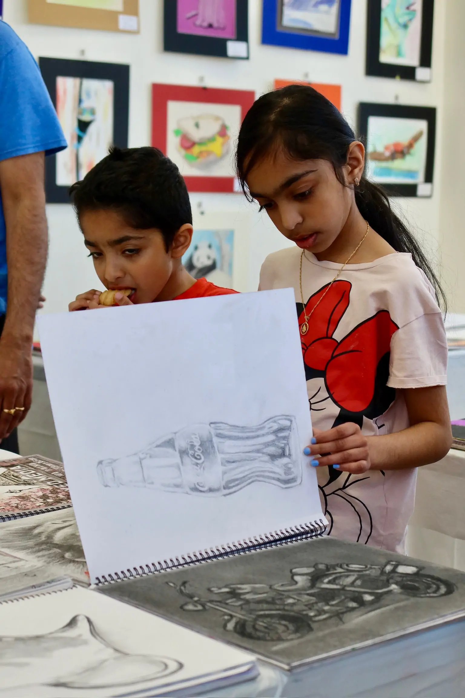 Two children at Aliki’s Art House looking at a sketchbook drawing during a youth art class.