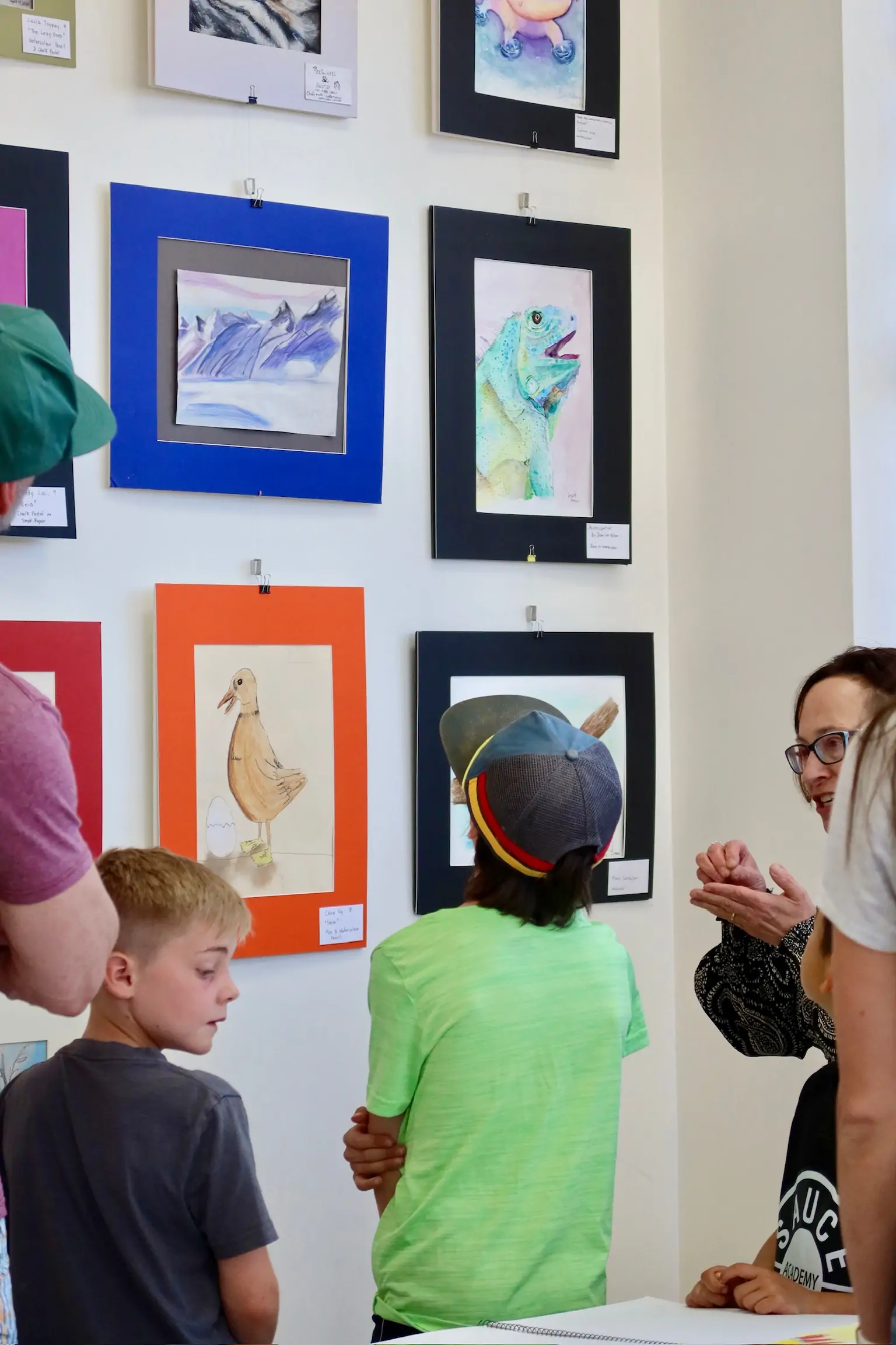 Children and parents viewing framed student artwork on the wall during the Aliki’s Art House showcase.