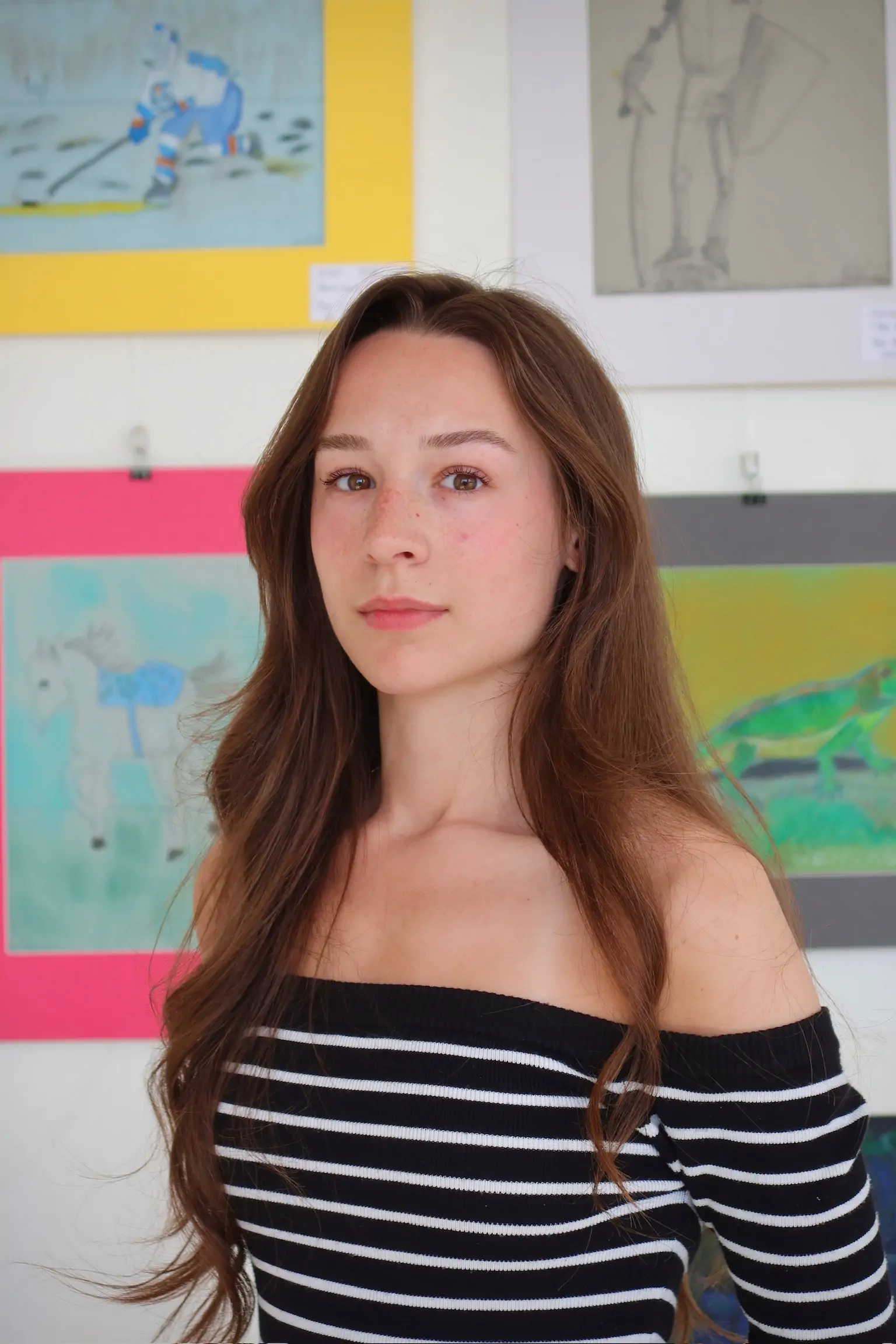 Annaka Didrikson, journalism student at SAIT and former AUArts fine arts student, standing in front of colorful artwork at Aliki’s Art House in Calgary