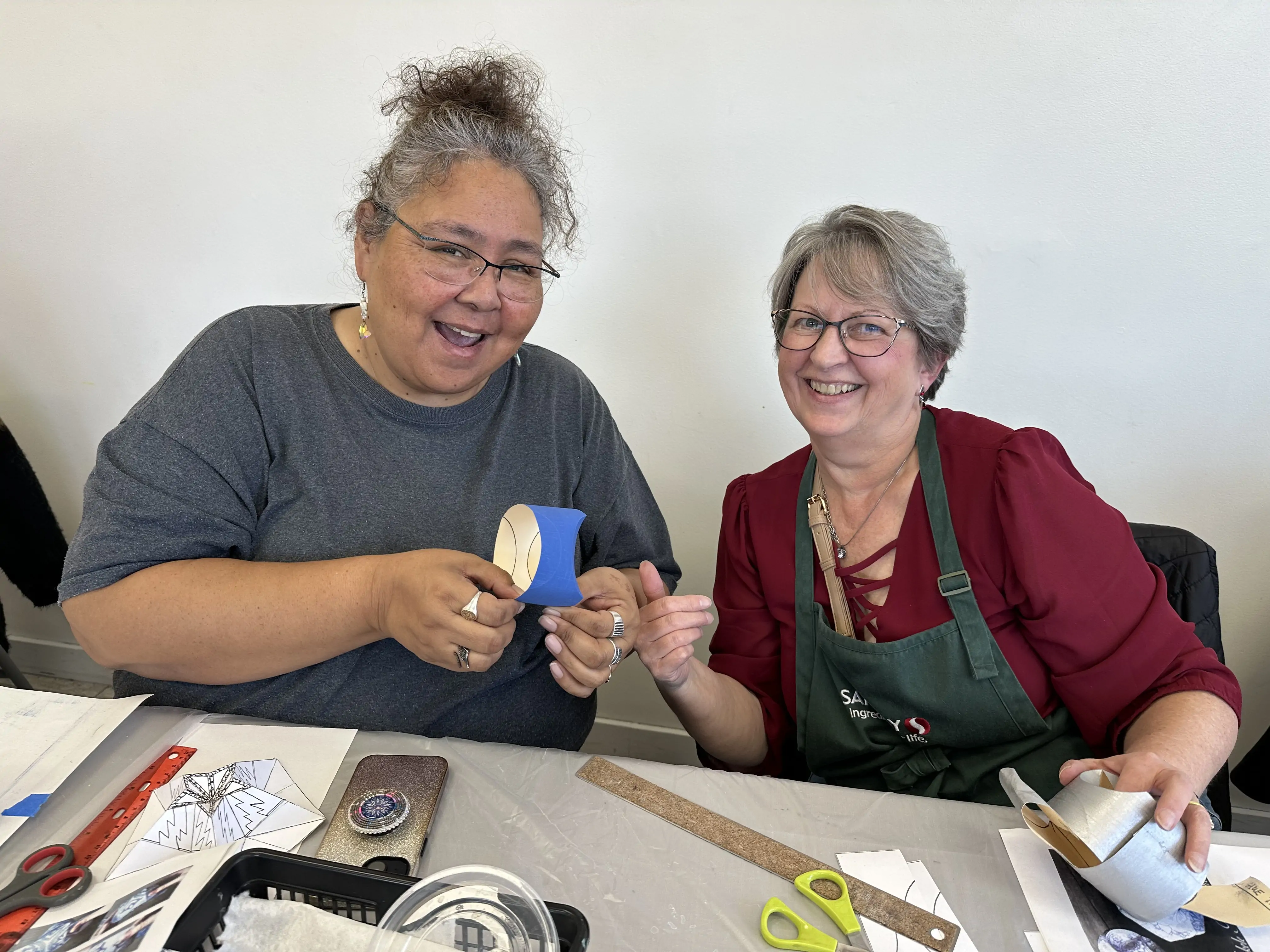 two adult students smiling and assembling paper sculptures during an art workshop at Aliki’s Art House in Calgary