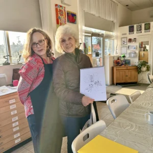 Art instructor Penny Atkins at Aliki’s Art House in Calgary standing with an adult student holding a bee drawing from the Drawing Fundamentals class