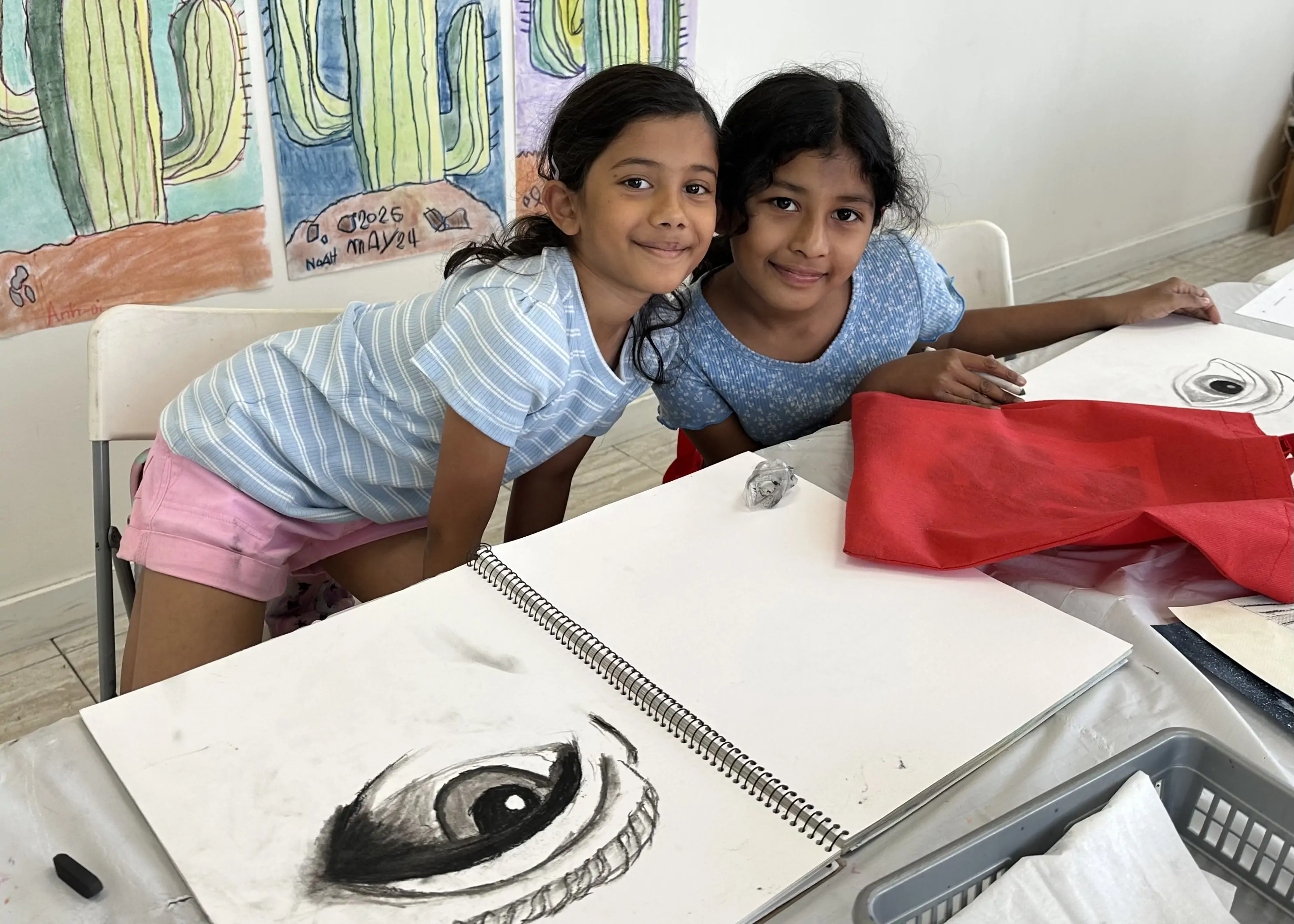 Two young students smiling and working on charcoal eye drawings together during an art class at Aliki’s Art House in Calgary